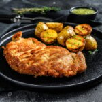 Breaded german weiner schnitzel with potatoes. Black background. Top view